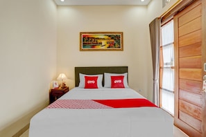 A hotel room with a bed, a nightstand with a lamp, a painting on the wall, and a wooden door.