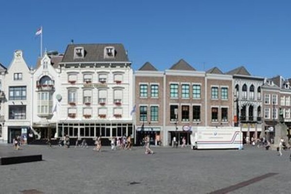 A public square with historic buildings, a bus, and people.