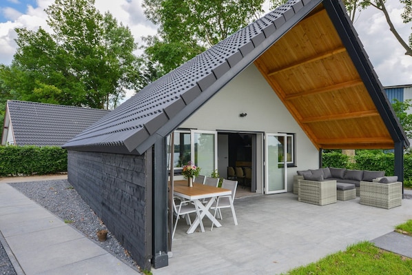 A modern house with a sloped roof, a patio with outdoor furniture, and a glass door leading to an interior space.