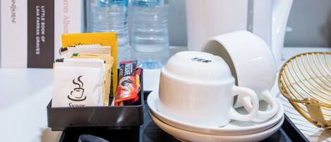 Ein Hotelzimmer mit einem ordentlich hergerichteten Frühstückswagen, der eine weiße Teekanne, Tassen und Wasserflaschen beinhaltet.