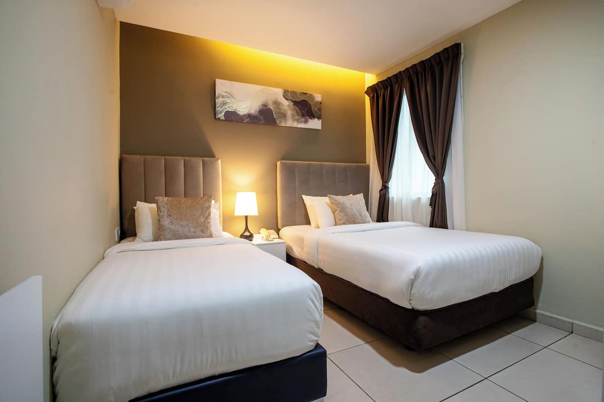 Habitación de hotel con dos camas, una mesita de noche con lámpara, un cuadro en la pared y una ventana con cortinas.