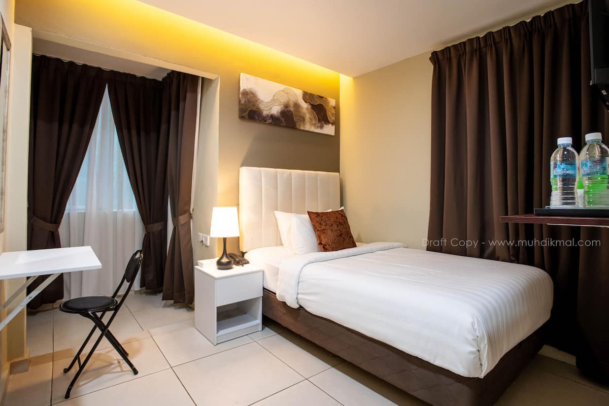 Habitación de hotel con cama, escritorio, silla, mesita de noche con lámpara y un cuadro en la pared.