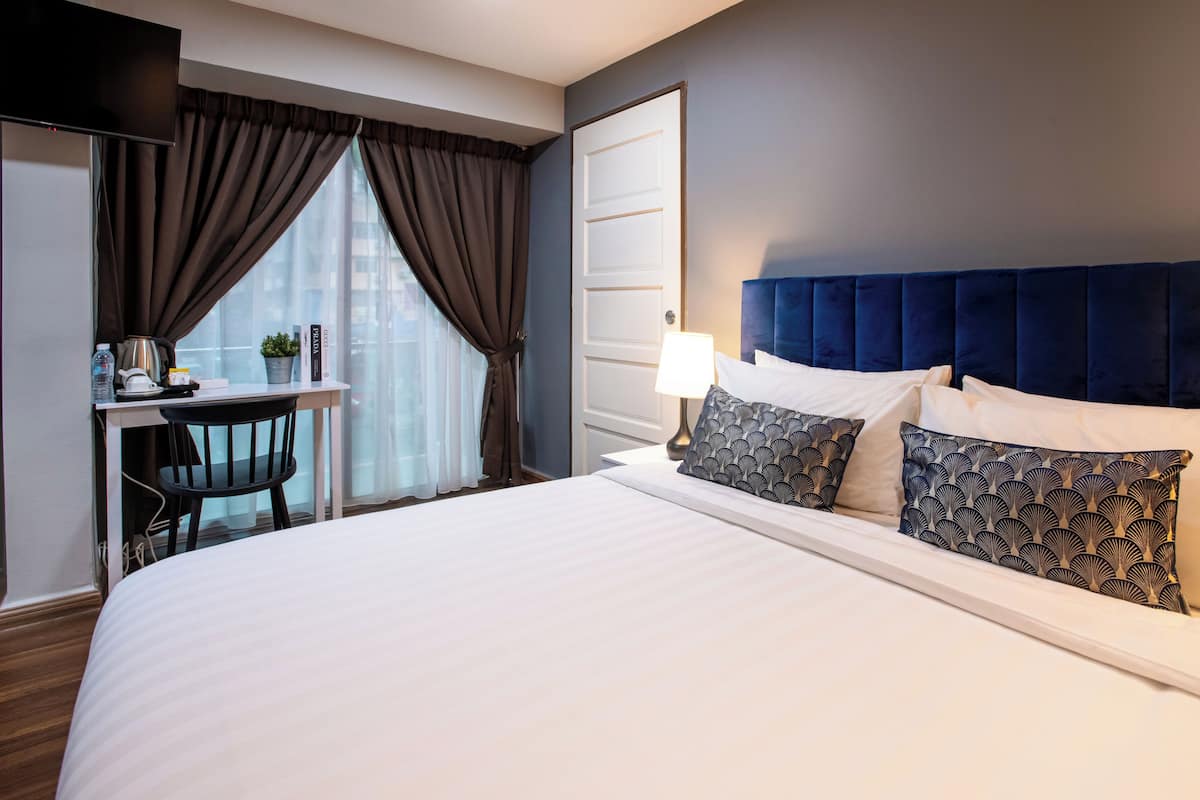 Habitación de hotel con cama, escritorio, silla, lámpara y ventana con cortinas.