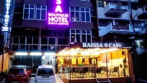 A hotel with a prominent neon sign, a cafe, and a parking area with cars. - Raissa Boutique Hotel (Kuala Lumpur)