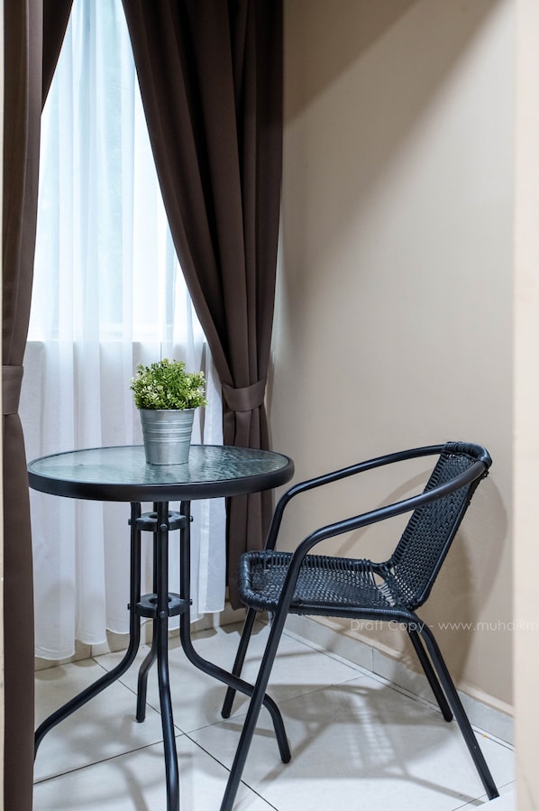 Una pequeña mesa redonda con una planta en maceta, una silla de mimbre negra y una ventana con cortinas.