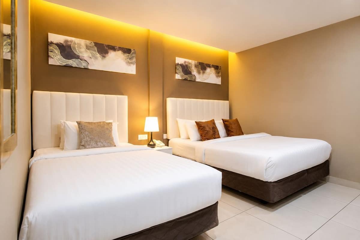 Habitación de hotel con dos camas, una mesita de noche con lámpara y obras de arte en las paredes.