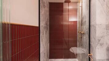 Une salle de bain moderne dotée d’une douche à parois de verre, de murs en marbre et d’un espace de douche carrelé de carreaux rouges.