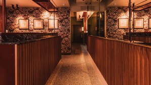 A hotel lobby with a wooden reception desk, framed artwork on the walls, and a carpeted floor. - The Sarah by Urban Rest (Darlinghurst)