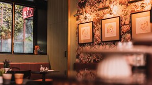 A restaurant interior with a floral wallpaper, framed artwork on the wall, a 'SUKI' sign outside, and a seating area with tables and chairs. - The Sarah by Urban Rest (Darlinghurst)