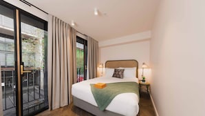 A hotel room with a large bed, a sliding glass door to a balcony, and a small bedside table with a lamp. - The Sarah by Urban Rest (Darlinghurst)