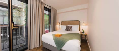 A hotel room with a large bed, a sliding glass door to a balcony, and a small bedside table with a lamp.