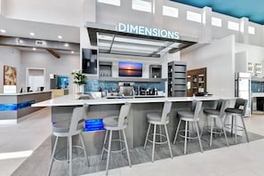 A modern bar area with a check-in counter, bar stools, and a TV screen displaying a sunset. - Chic and Cozy Townhouse near Disney with Resort & Waterpark Access - 824DR (Kissimmee)