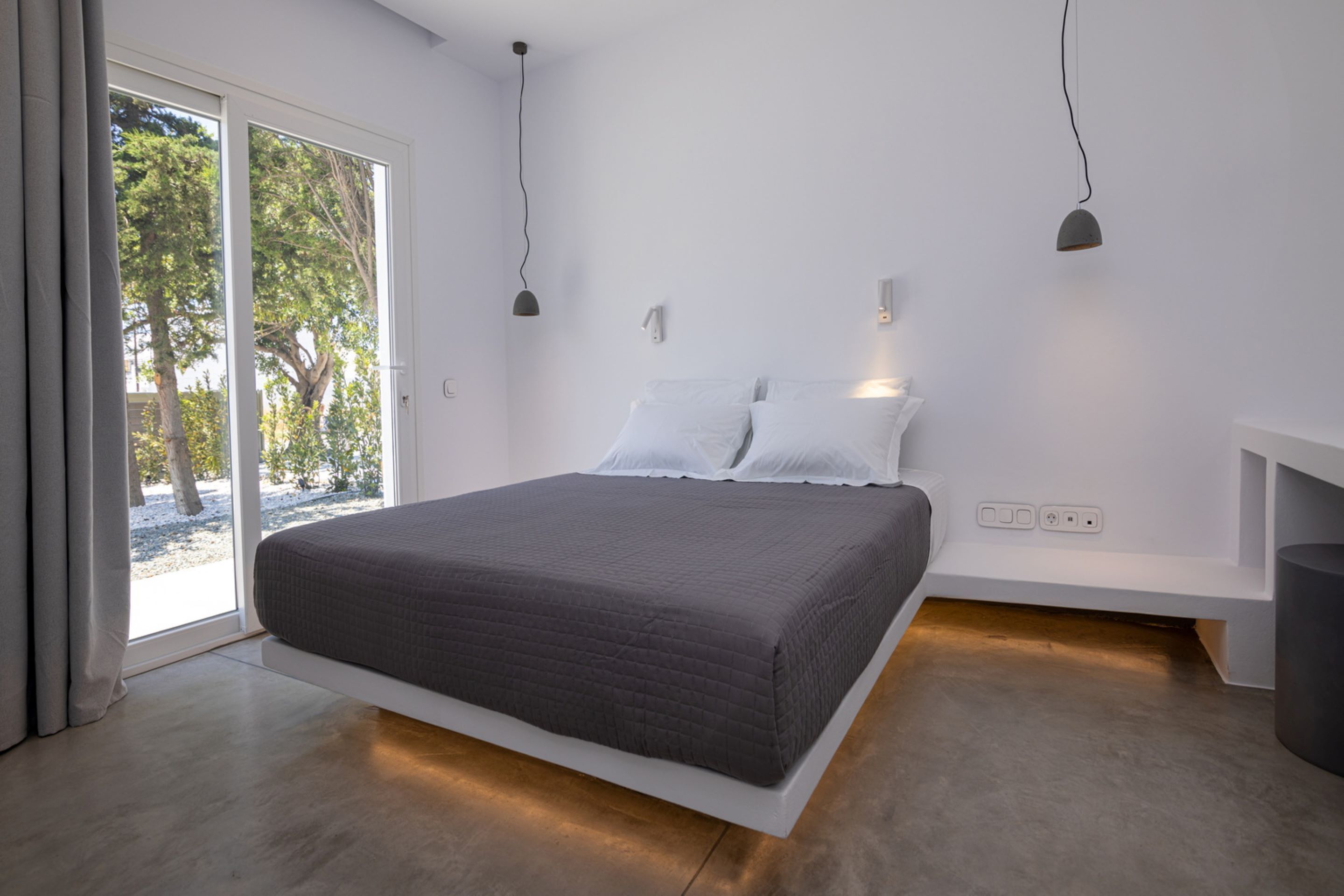 Un dormitorio moderno con una cama grande, mesitas de noche empotradas y un ventanal corredero que da a un espacio exterior.