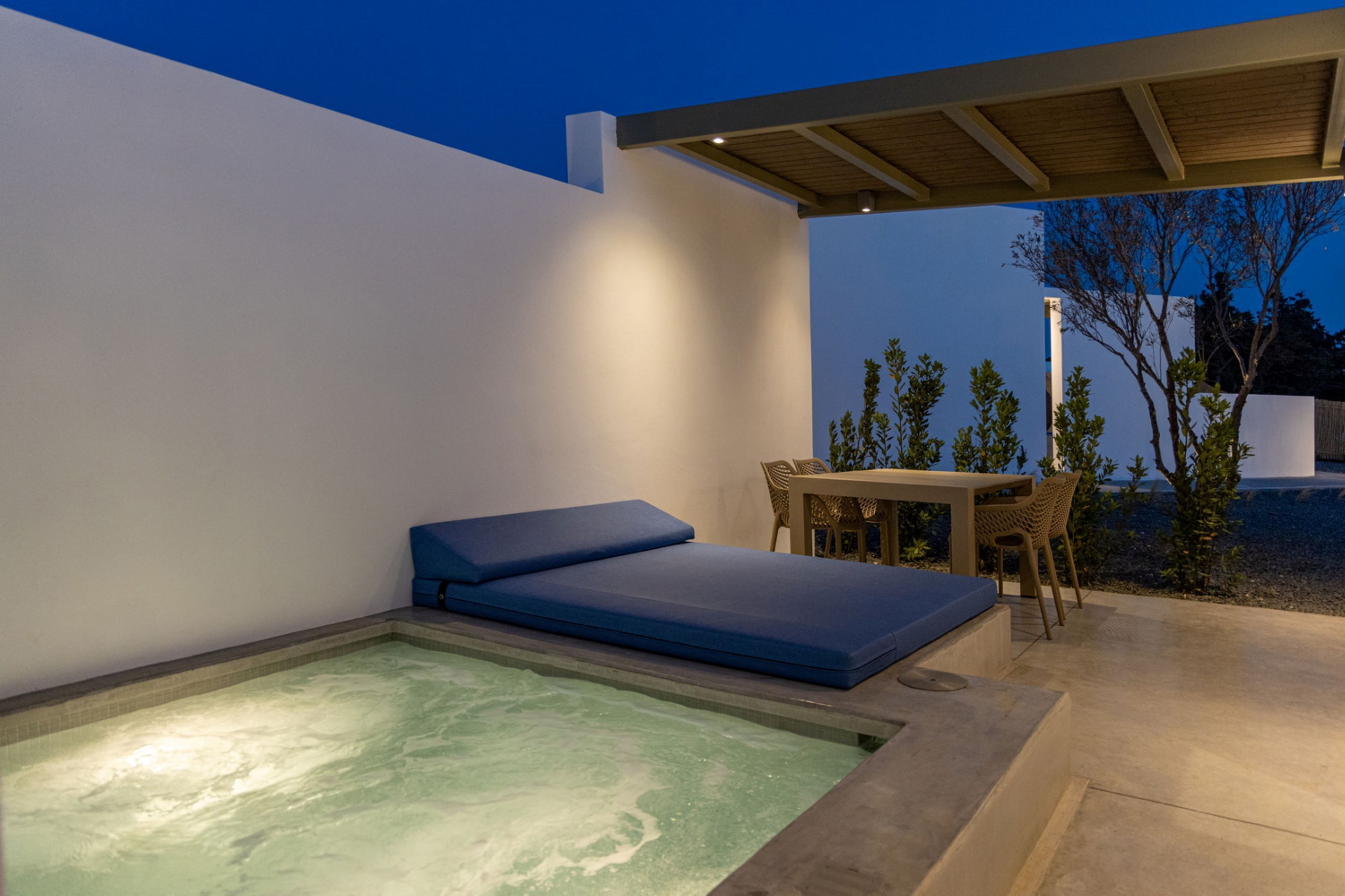Uma área externa moderna com hidromassagem, um banco acolchoado azul, uma mesa e cadeiras.