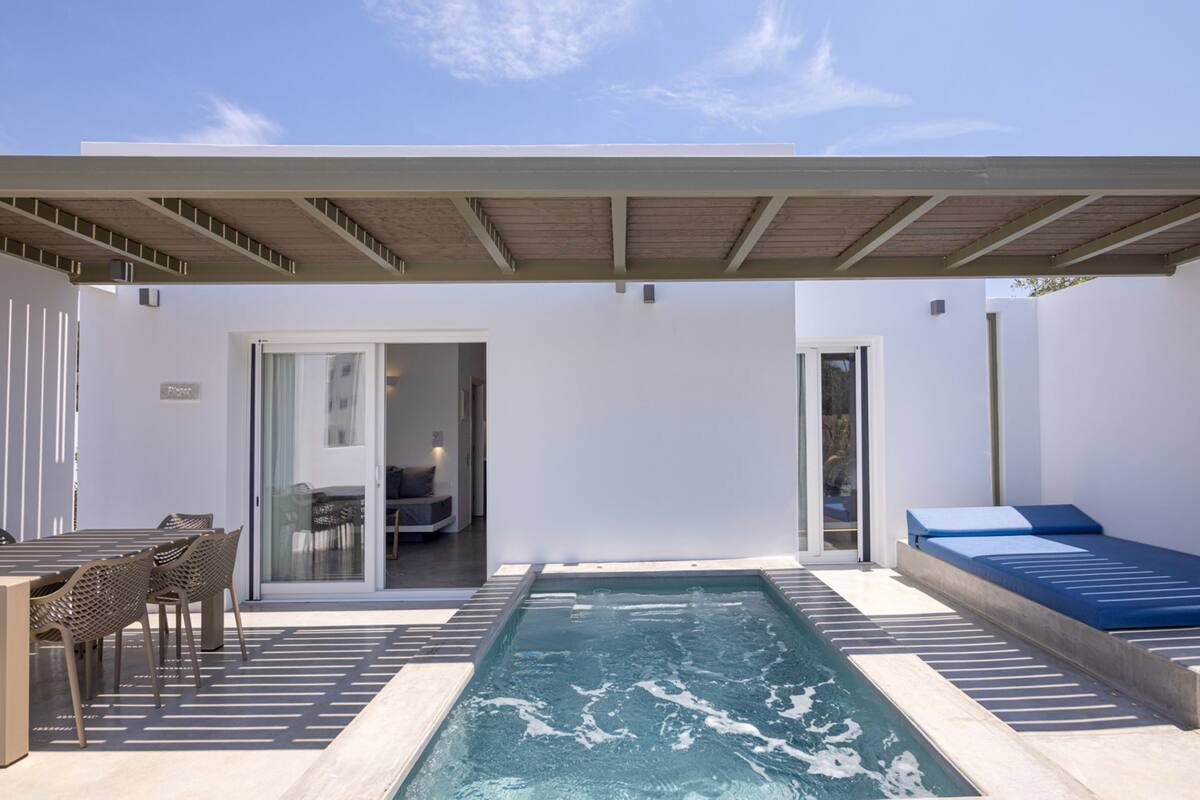 A modern outdoor pool area with a covered seating area, a lounge chair, and a dining table with chairs.
