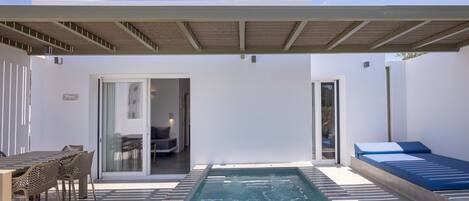 A modern outdoor pool area with a covered seating area, a lounge chair, and a dining table with chairs.