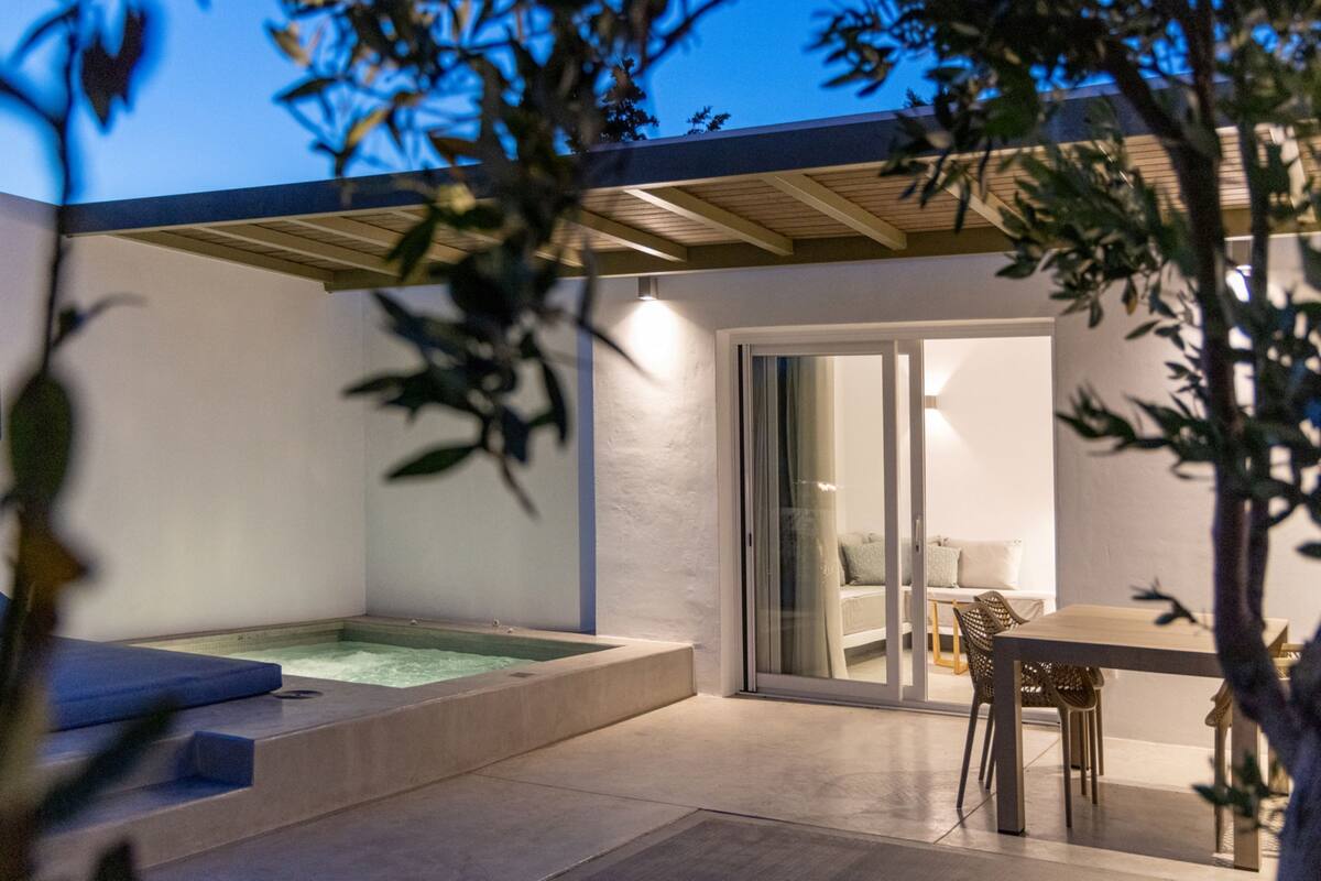 A modern outdoor patio with a hot tub, a dining area, and a sliding glass door leading to an interior space.