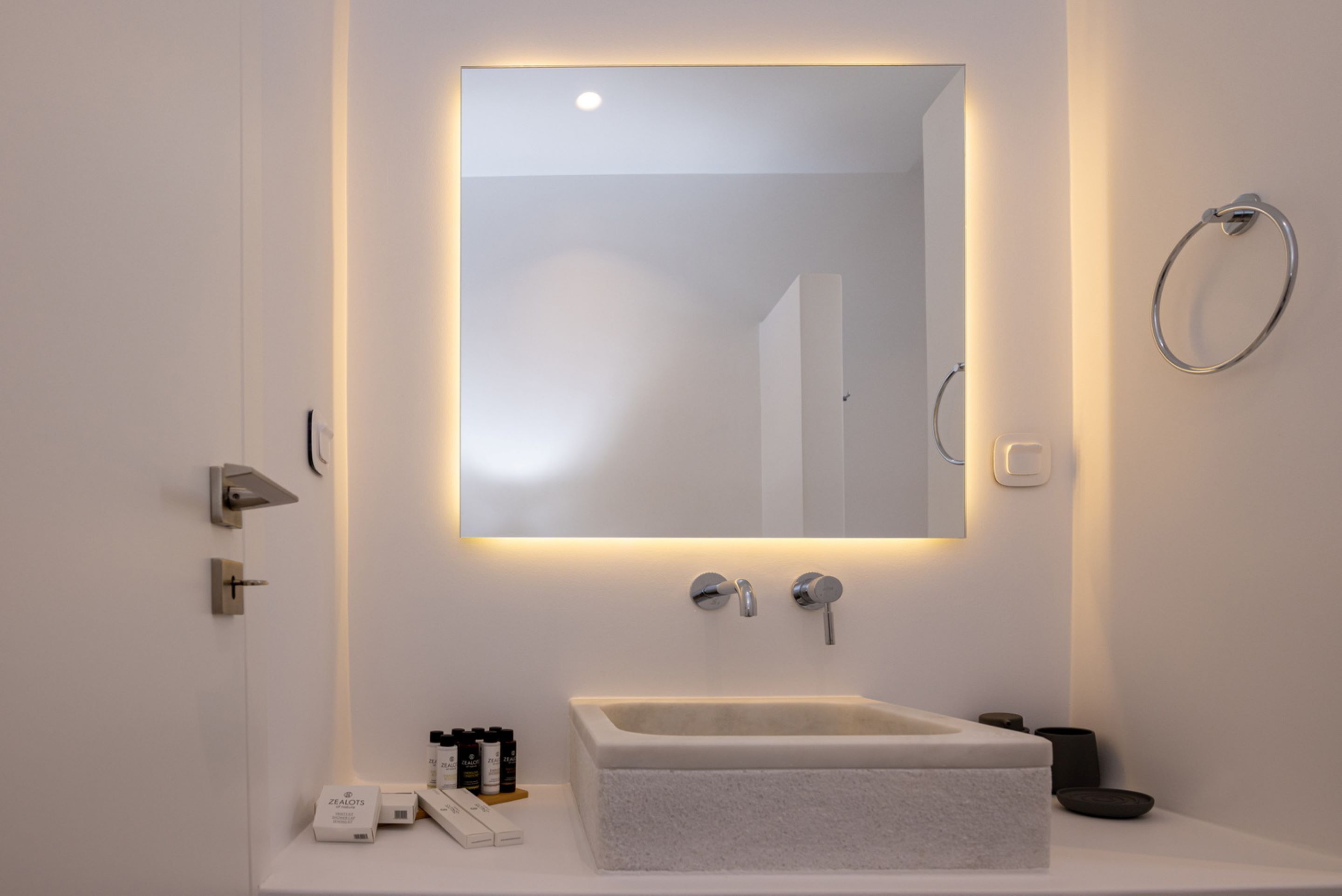 Een moderne badkamer met een rechthoekig wastafeltje, een grote spiegel en een handdoekhouder aan de muur.