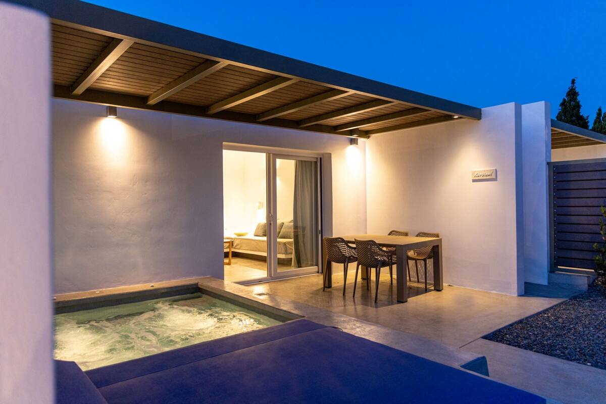 A modern outdoor patio with a hot tub, a dining area with chairs, and a covered seating area.