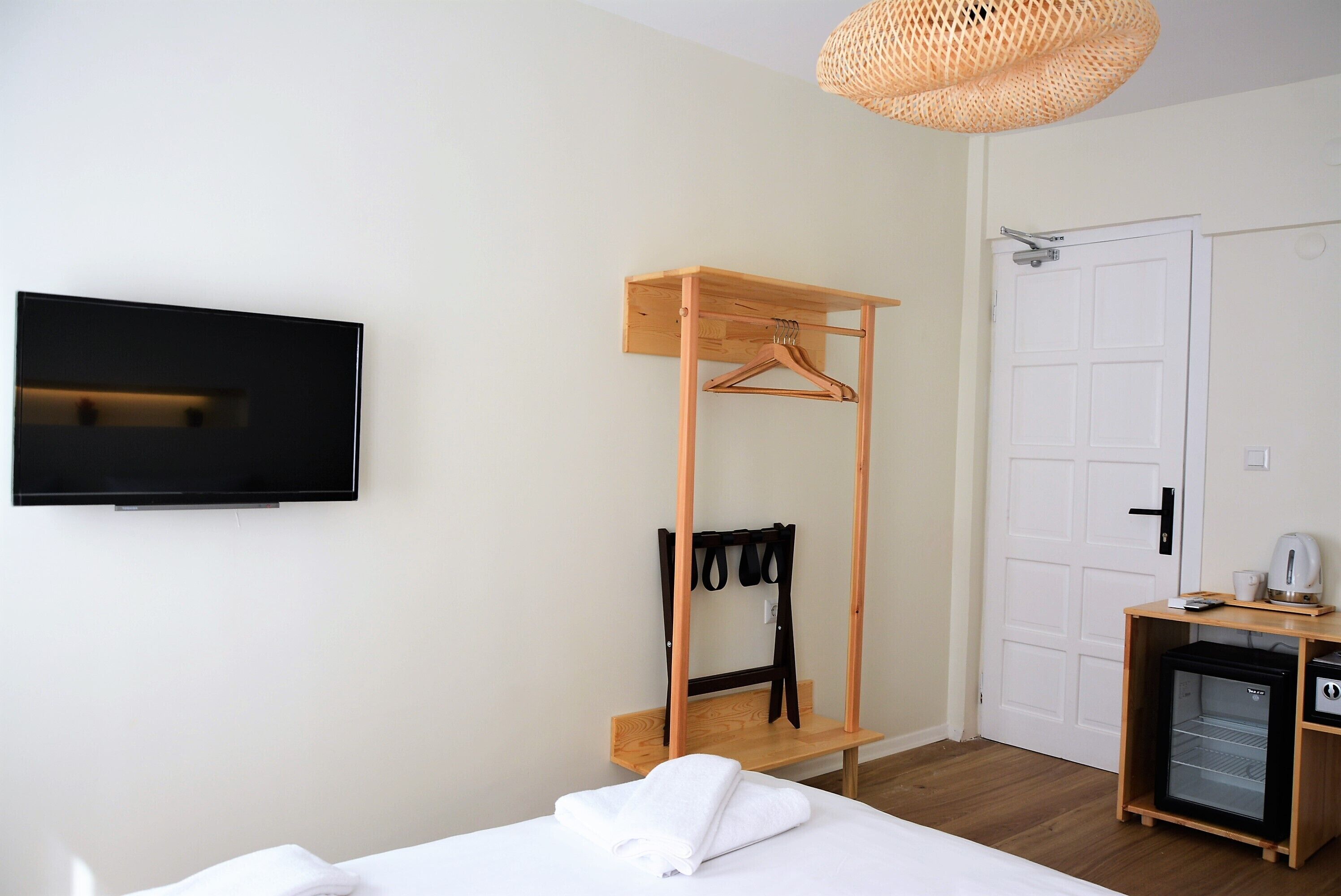 A bedroom with a bed, a wooden hangerboard, a television, a door, and a small refrigerator.