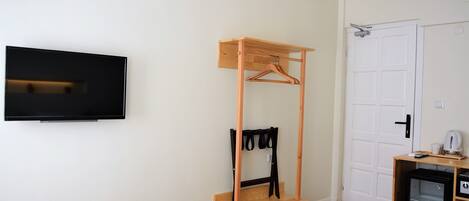 A bedroom with a bed, a wooden hangerboard, a television, a door, and a small refrigerator.
