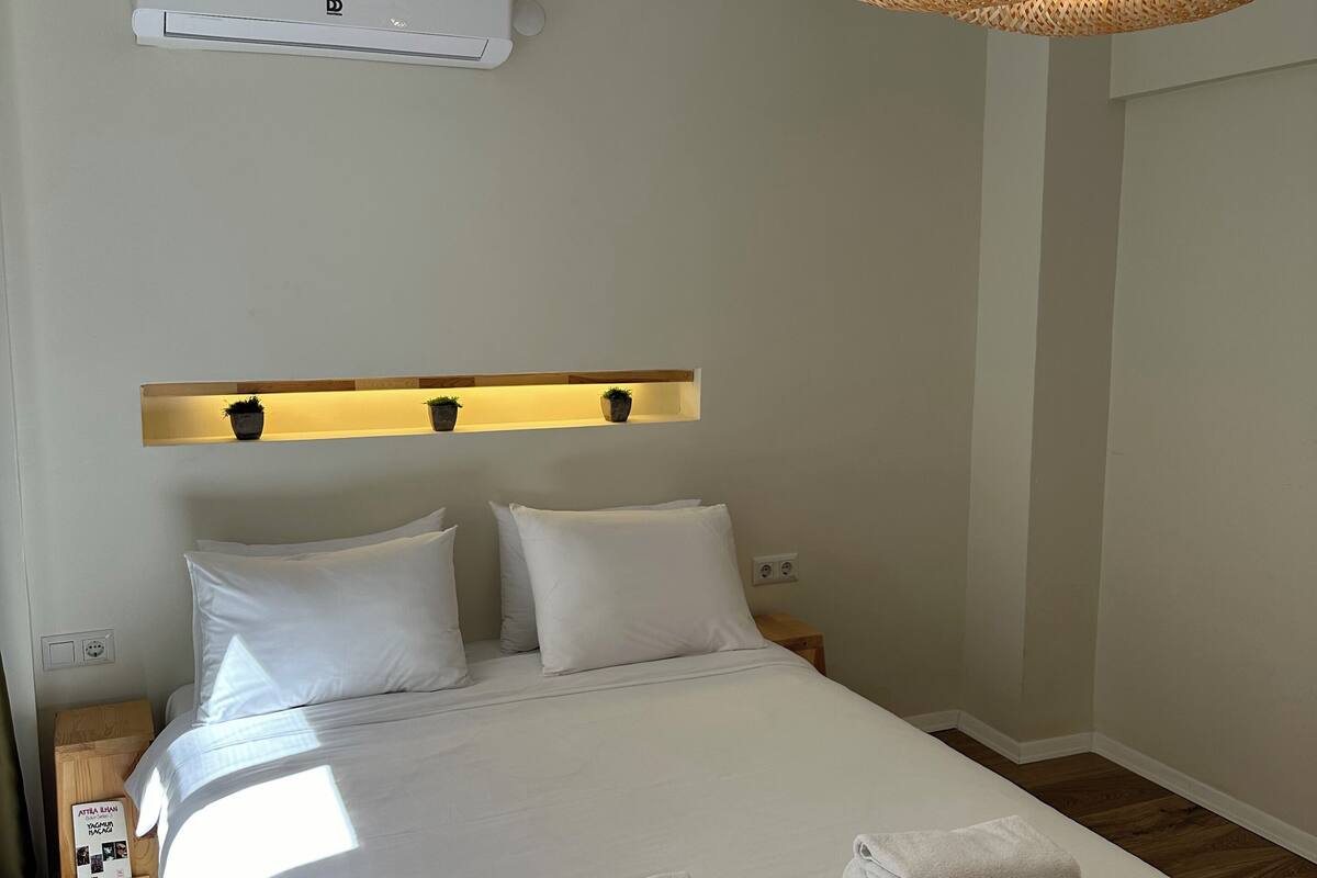 A neatly made bed with white linens, a bedside table with a lamp, and a hanging woven light fixture.