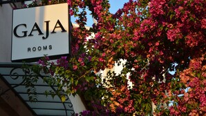 Skilt med teksten "Gaja Rooms" og udsigt til buganvilleaf blomster.