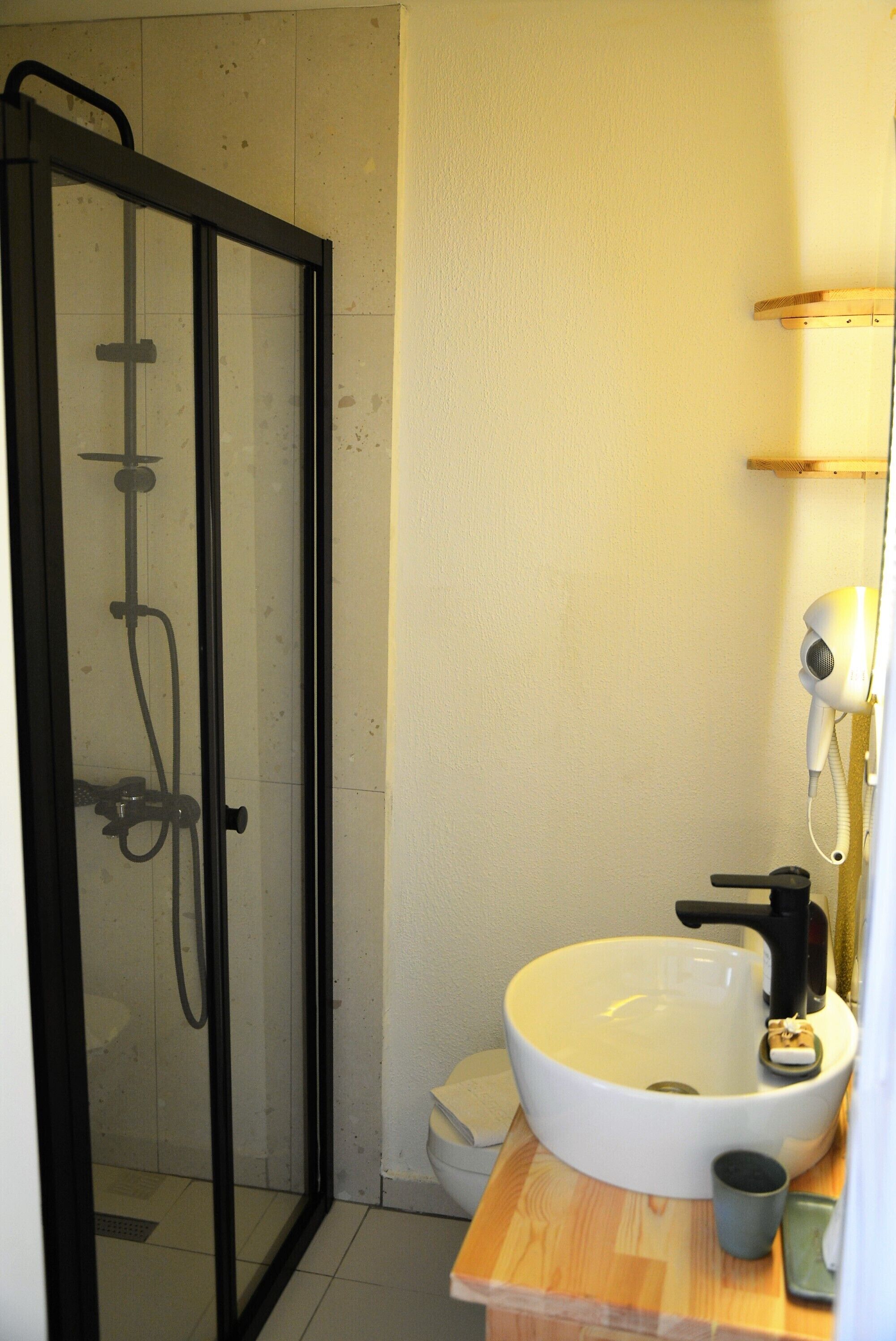 A bathroom with a glass-enclosed shower, a white sink with a black faucet, and a wooden countertop.