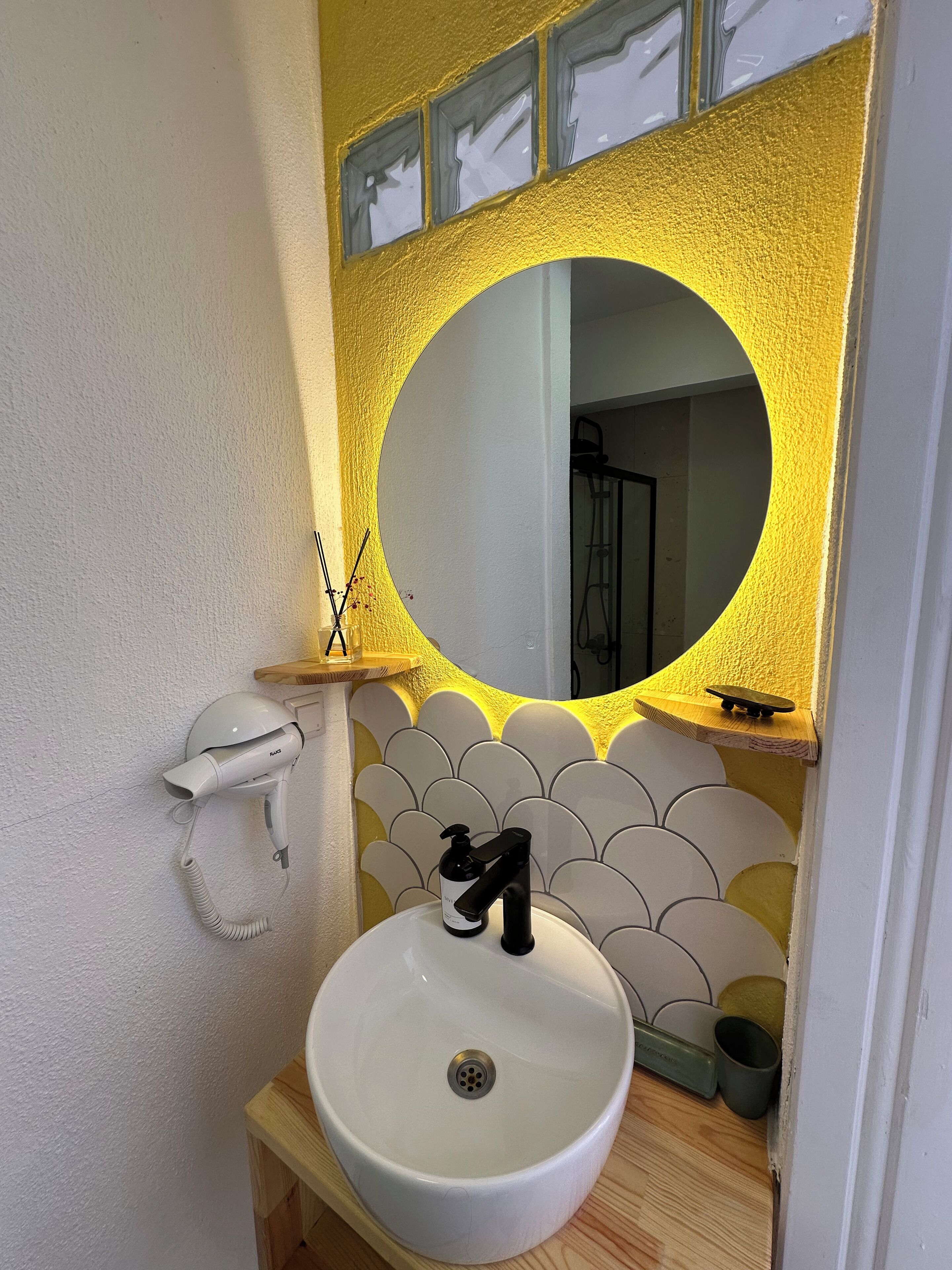 A bathroom with a white sink, a mirror with a yellow frame, and a towel dispenser.
