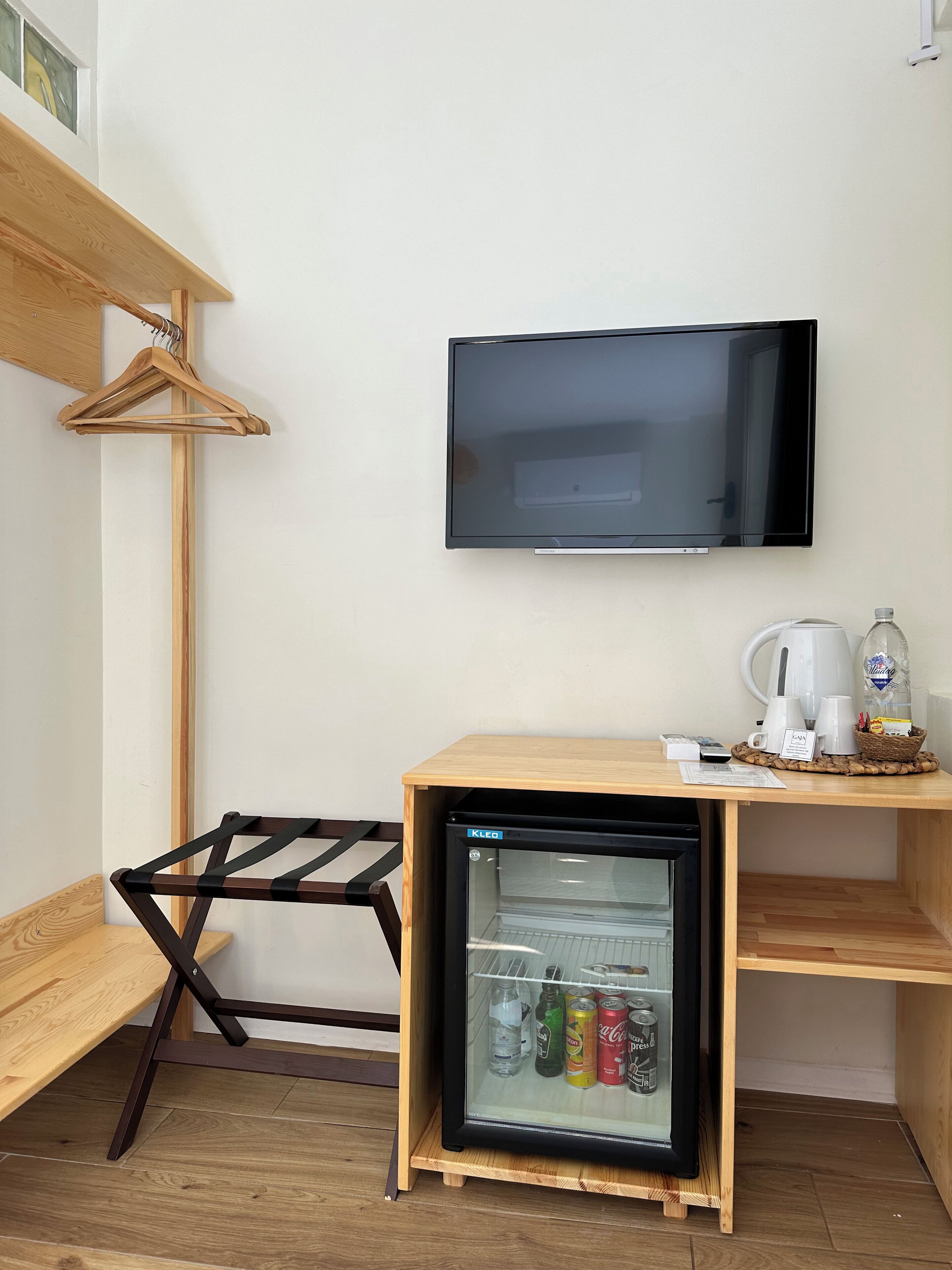 A compact room with a wooden desk, a small refrigerator, a television, and a drying rack.