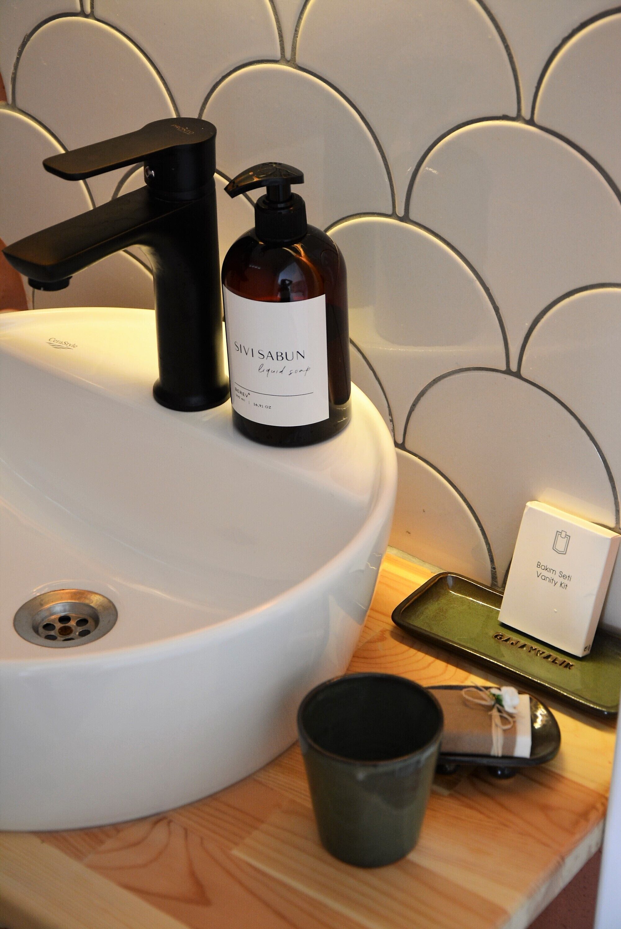 A bathroom sink with a black faucet, a bottle of SIVISABUN liquid soap, a small tray with a box labeled "Bokim Self Vanity Kit," and a black mug.