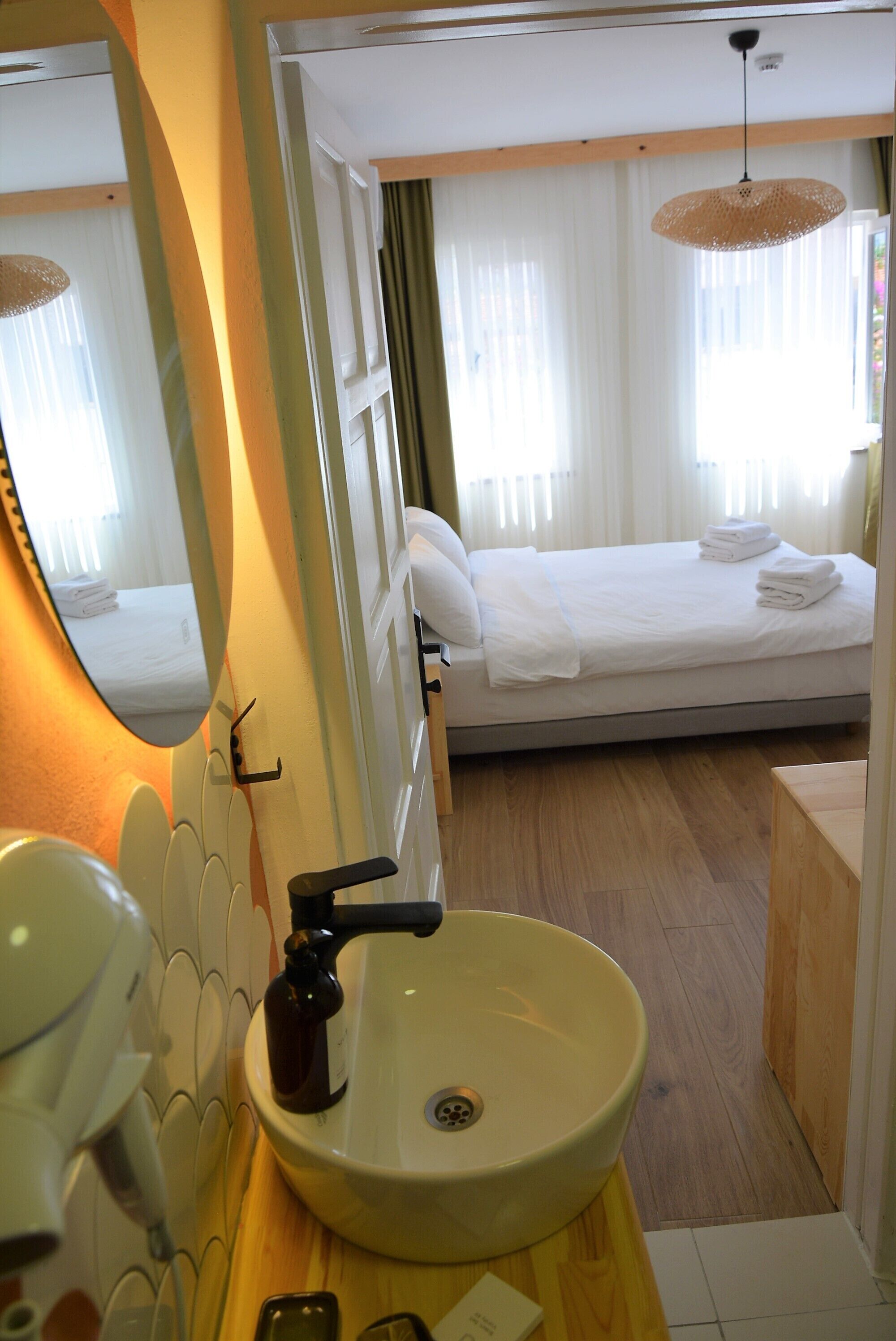 A hotel bathroom with a sink, mirror, and a bed visible through an open door.