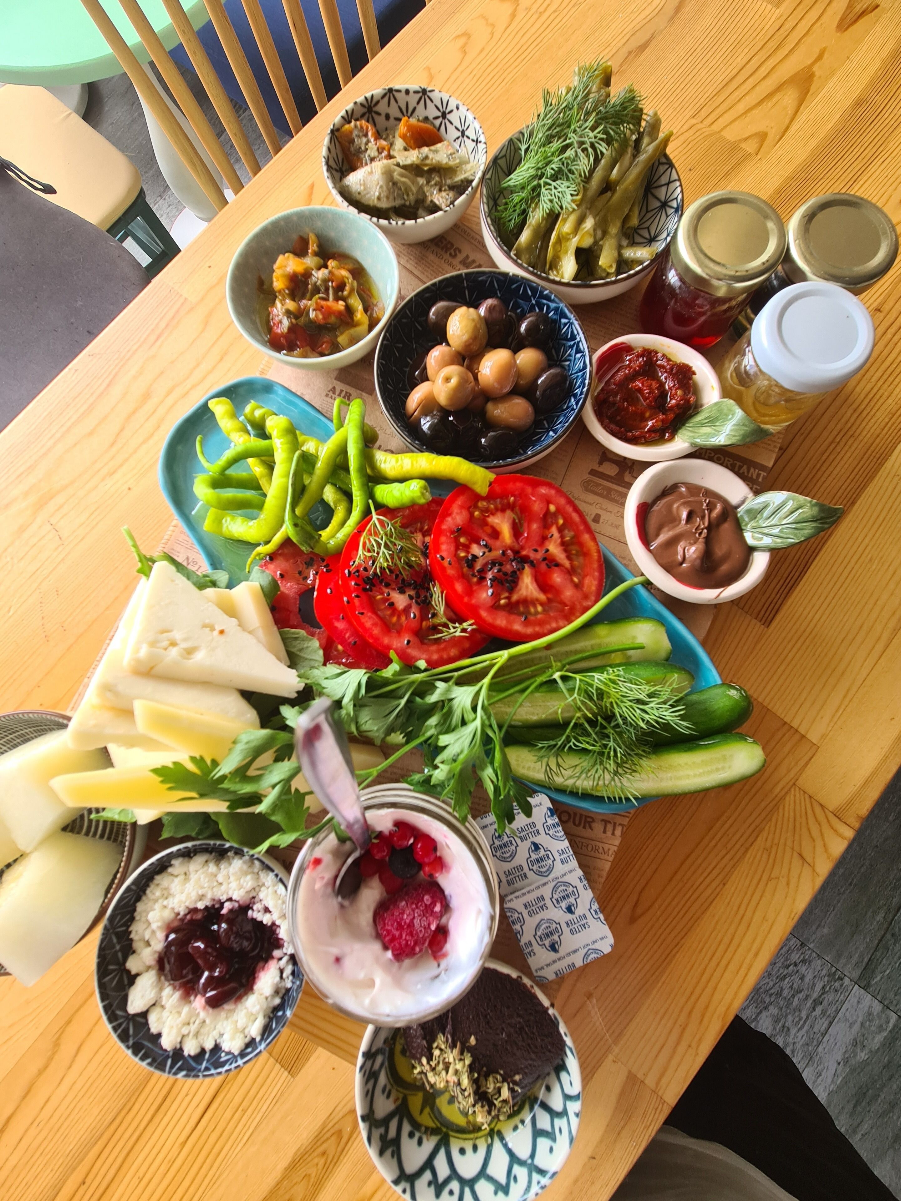Ein Holztisch mit verschiedenen Speisen darunter Käse, Tomaten, Gurken, Oliven und eine Schüssel Joghurt.