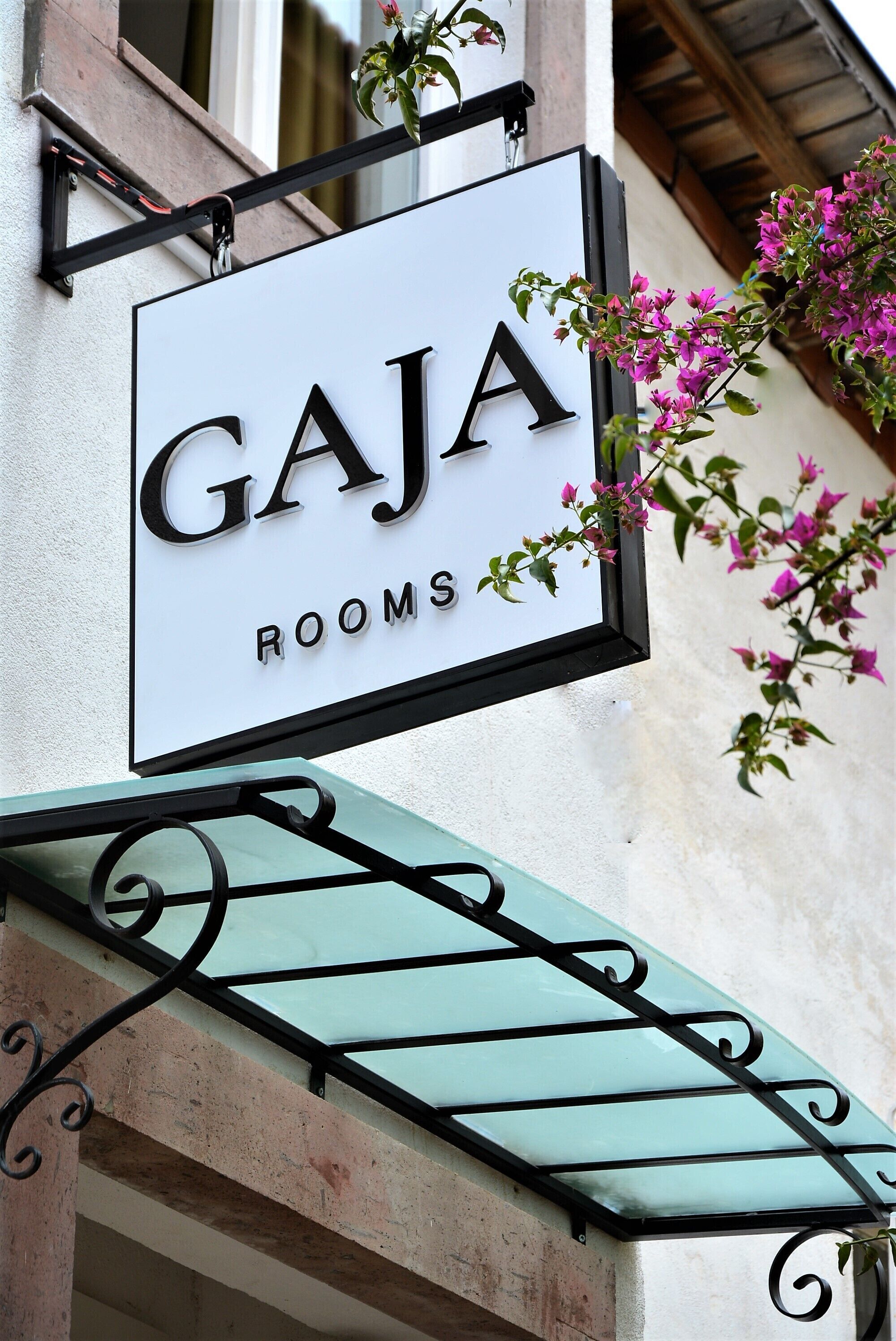 A sign for "Gaja Rooms" with a balcony and bougainvillea flowers.