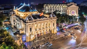 Um edifício histórico com arquitetura clássica, uma cúpula central e uma grande praça aberta com carros e pessoas.