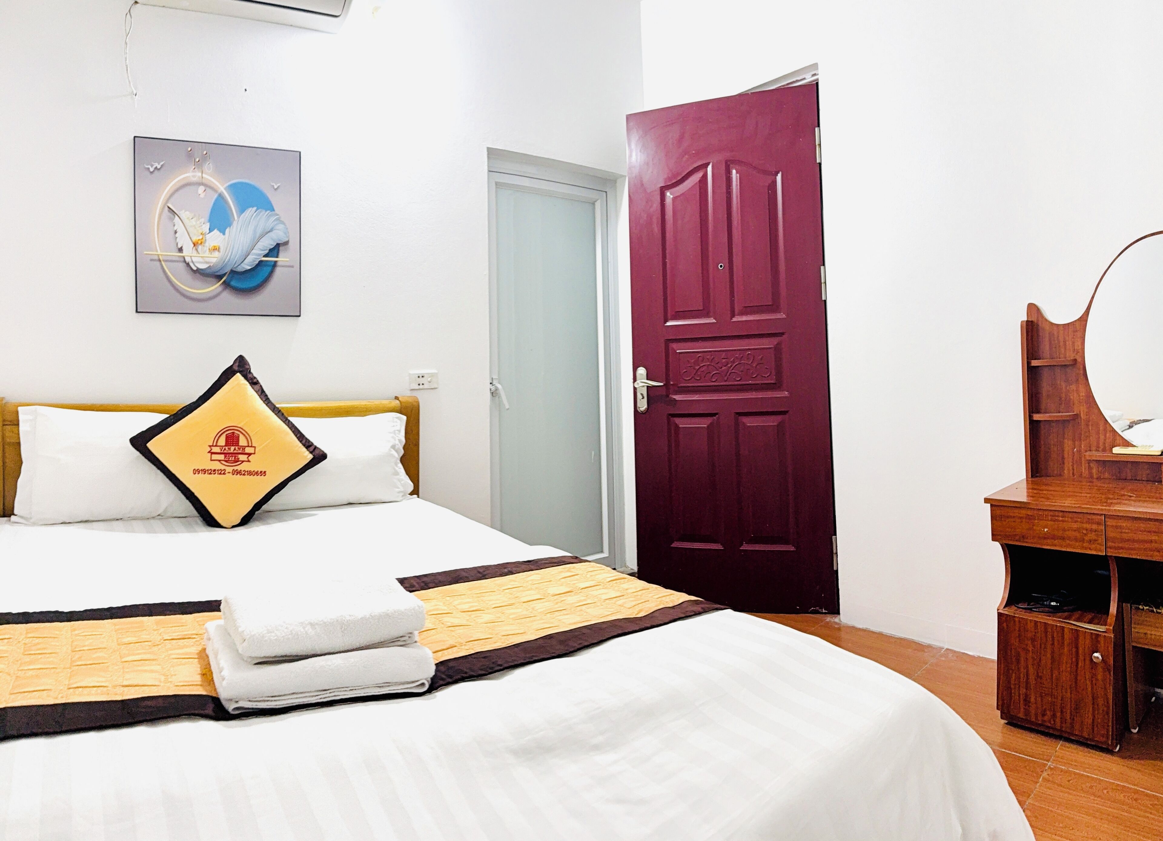 A hotel room with a bed, a wooden dresser, a mirror, and a door.
