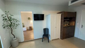 Una habitación con una televisión de pantalla plana en la pared, un mueble de madera, una silla y una planta en maceta.
