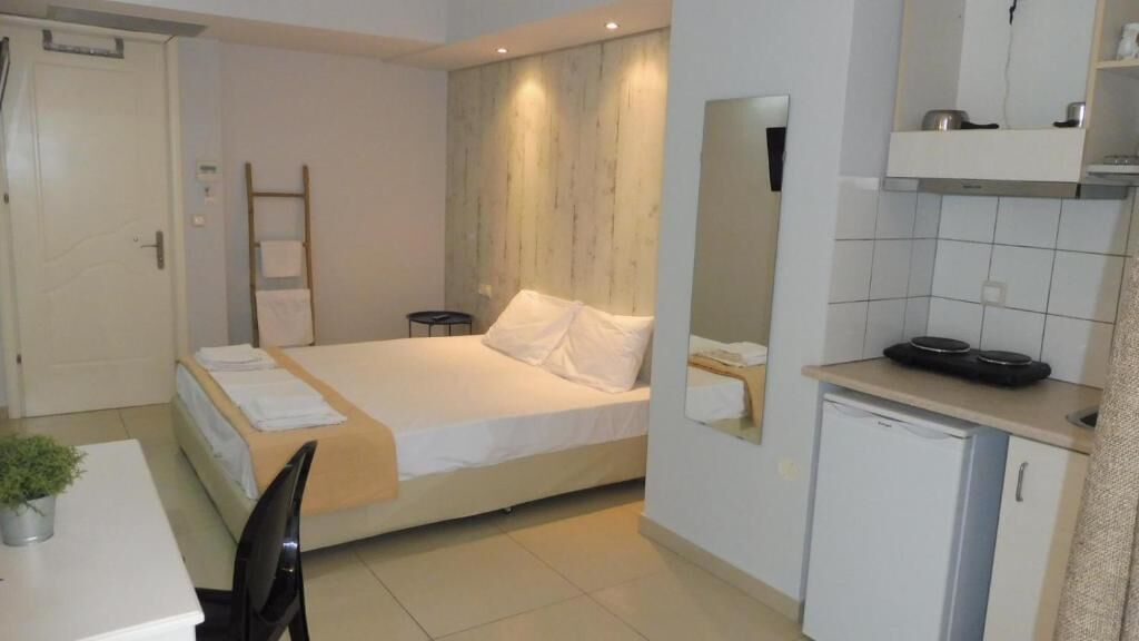 Una habitación de hotel pequeña y funcional con cama, escritorio, silla, kitchenette y baño.