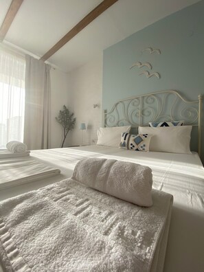 Una cama bien hecha con sábanas blancas y un cojín decorativo, una lámpara de noche y un aplique de pared.
