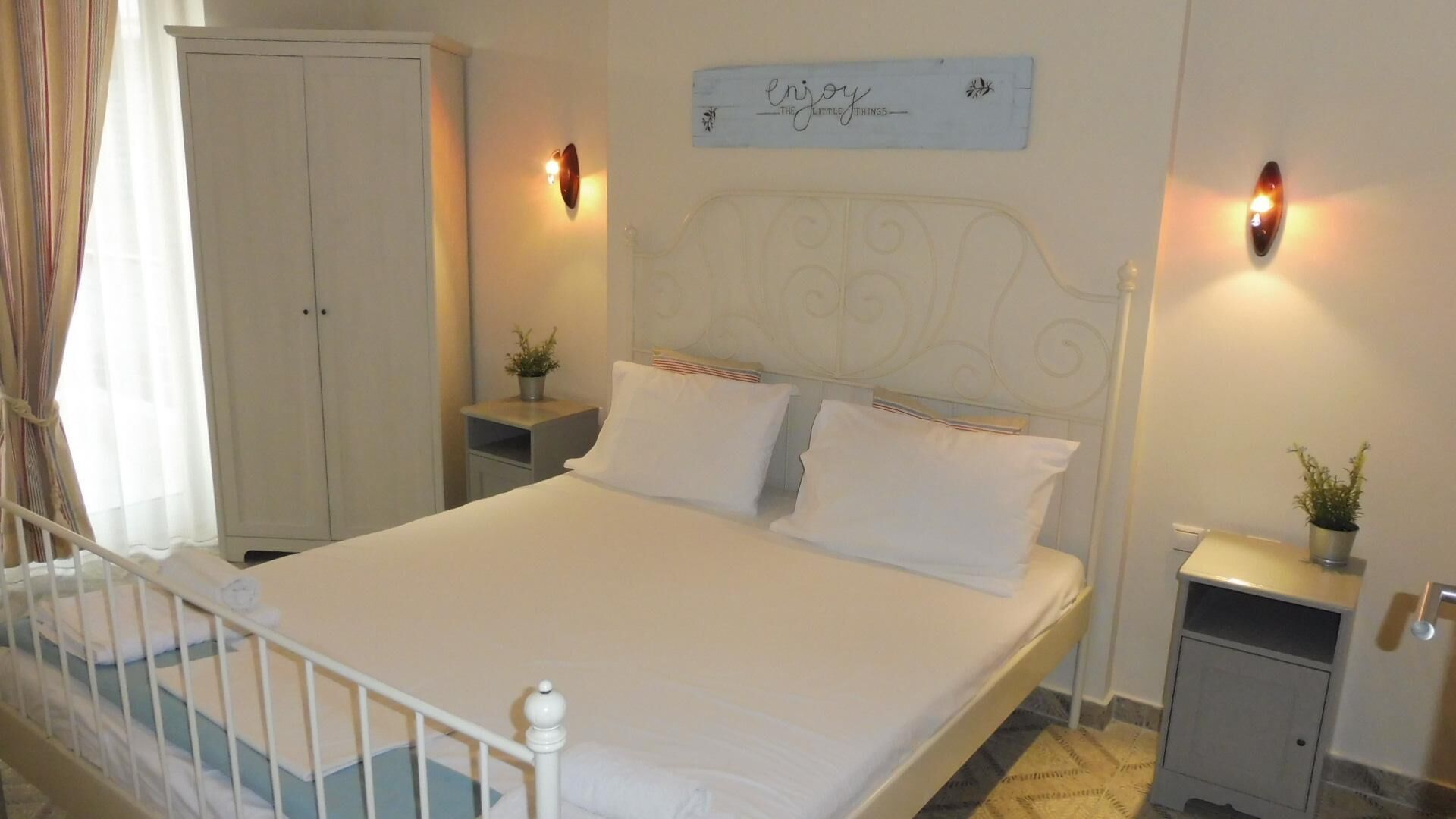 Una cama bien hecha con sábanas blancas, un cabecero con diseño decorativo, mesitas de noche con lámparas, un armario y un cartel en la pared.