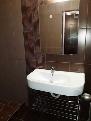 A bathroom with a white sink, a mirror, and brown tiled walls. - Klio Apartments and Studios (Dio-Olympos)
