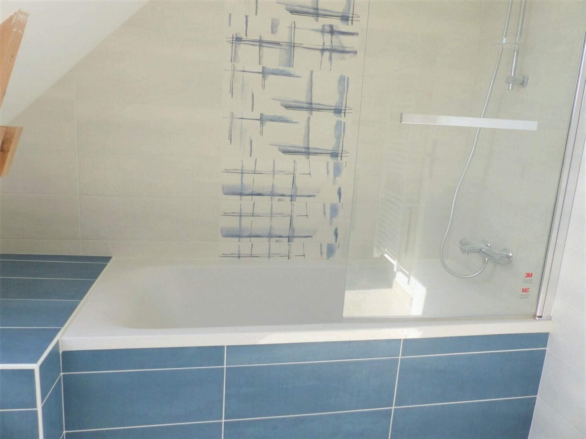 A bathroom with a glass-enclosed shower, blue tiles, and a visible 3M product label.