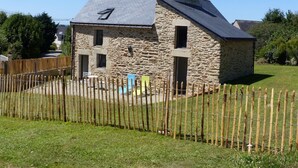 Una casa in pietra con tetto spiovente, un cortile recintato e cielo sereno.