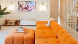A modern living room with a large orange sectional sofa, a white wall with a floral painting, and a staircase with wooden railings. - Nevada City Cabin Pups and Long Stays Welcome (Nevada City)
