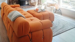 A cozy living room with a large sectional sofa, a brick fireplace, and a large window offering a view of the outdoors. - Nevada City Cabin Pups and Long Stays Welcome (Nevada City)