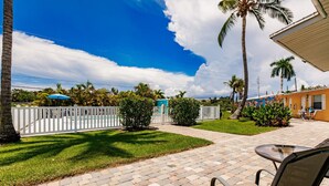 A patio area with a brick floor, outdoor seating, and a pool in the background. - Cottage Home by Beaches, Golf & More! Heated Pool! (Fort Myers)