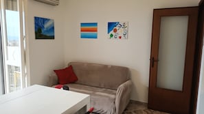A room with a beige sofa, a white table, and a wooden door. There are three paintings on the wall. - Top Floor Aparthotel Bentivoglio (Catania)