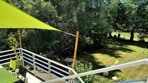 Ein überdachter Außenbereich mit Tisch und Stühlen, einer Treppe und Blick auf einen grünen Rasen mit Bäumen.