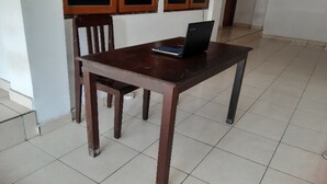 Une table en bois avec un ordinateur portable et un livre, une chaise en bois et un sol carrelé.