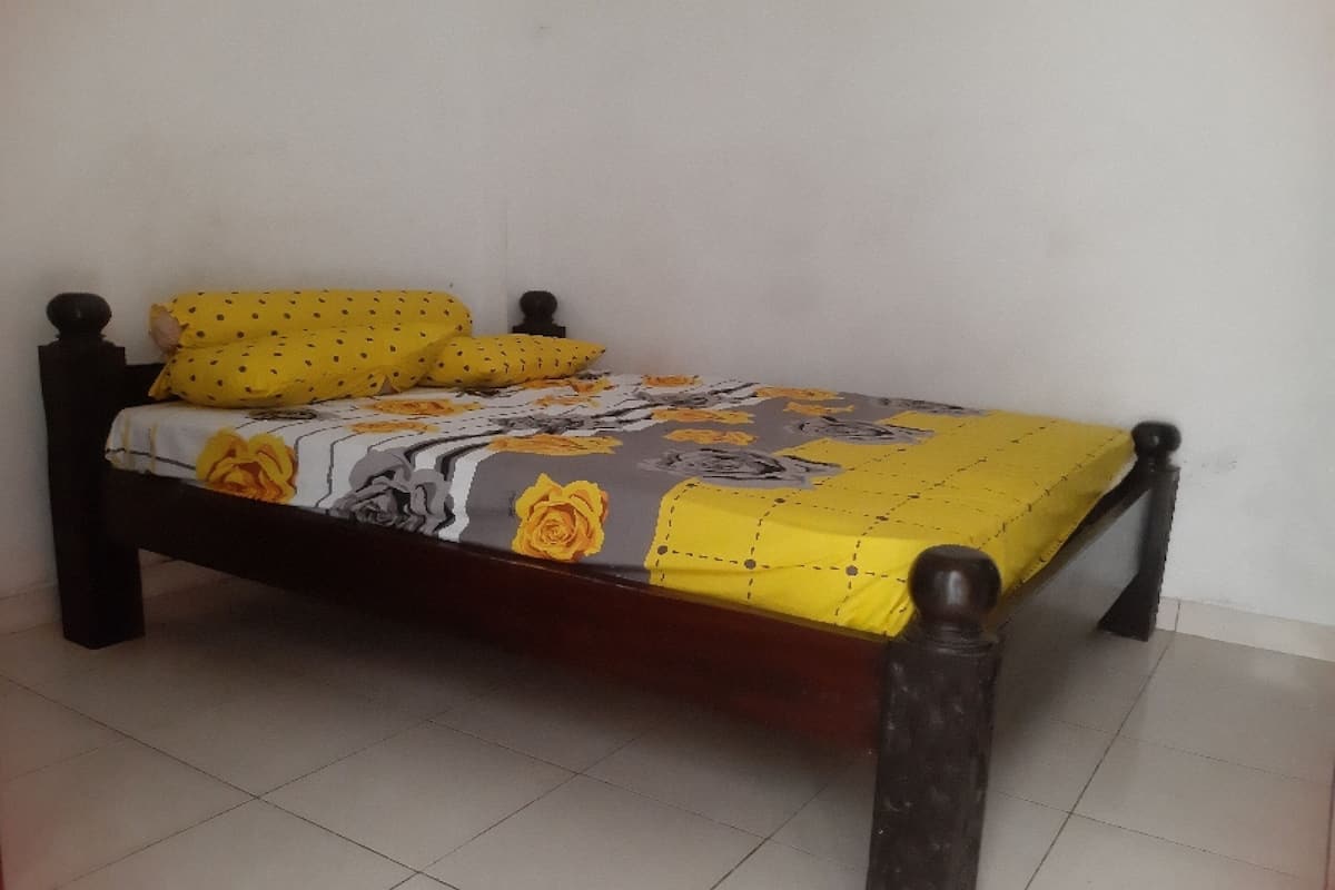 A bed with a floral bedspread and two pillows, a wooden headboard, and a tiled floor.